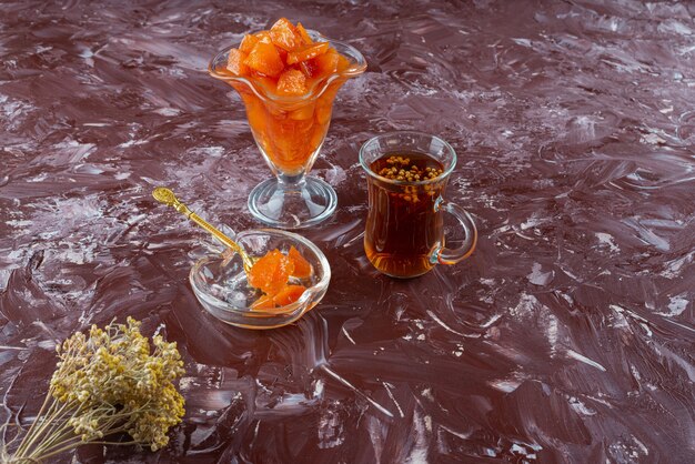 Verre de confiture de coings et verre de thé noir sur table.