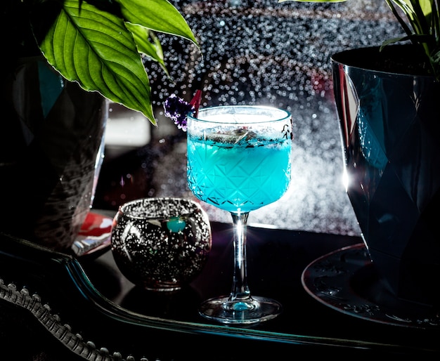 verre en cristal avec cocktail bleu garni de pétales de rose