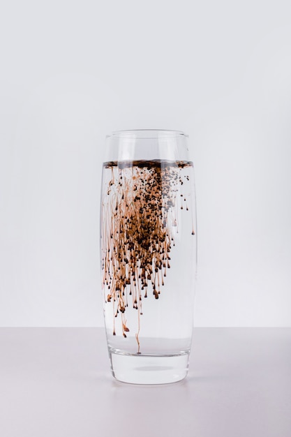 Verre d'eau avec un liquide foncé sur un mur blanc.