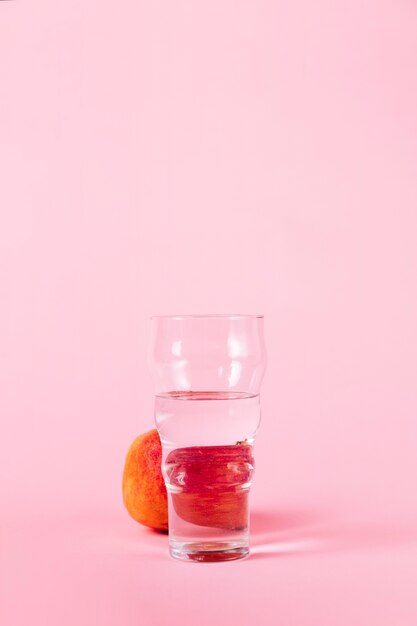 Verre d'eau et de nectarine sur fond rose