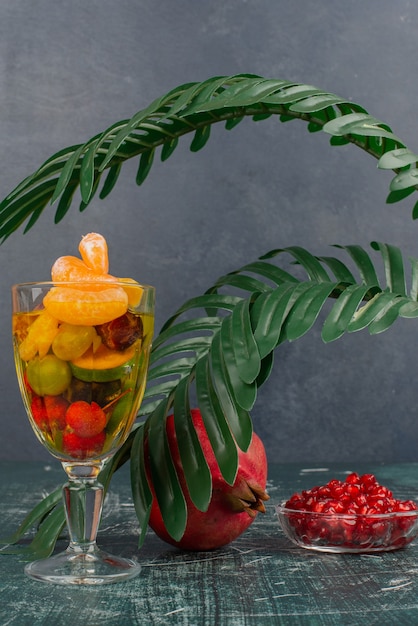 Photo gratuite verre de fruits mélangés et grenade avec graines sur table en marbre.