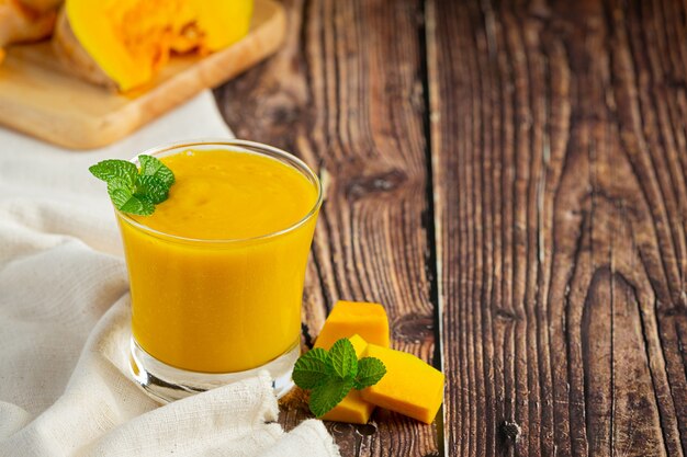 Un verre de jus de citrouille et de citrouilles crues hachées place sur un plancher en bois