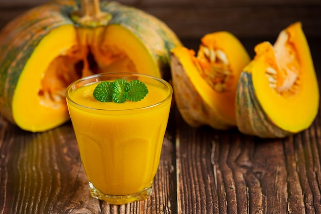 Un verre de jus de citrouille et de citrouilles crues hachées place sur un plancher en bois