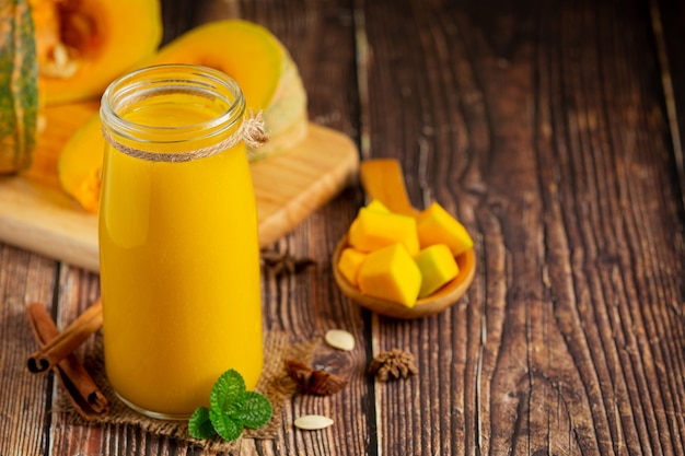 Photo gratuite un verre de jus de citrouille et de citrouilles crues hachées place sur un plancher en bois