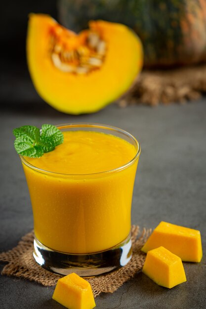 un verre de jus de citrouille et de citrouilles crues hachées sur un sol sombre