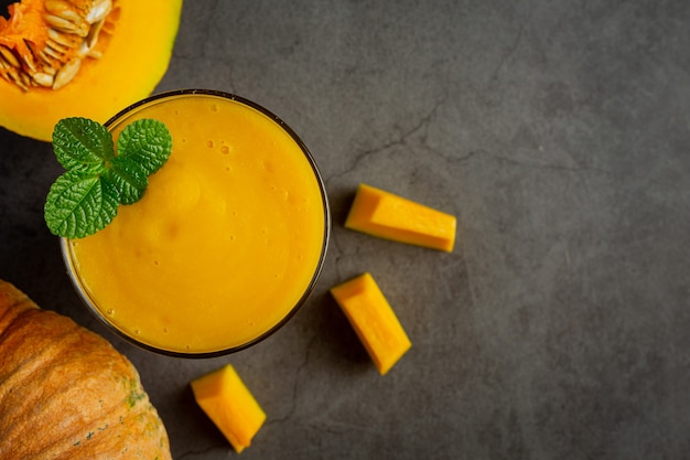 un verre de jus de citrouille et de citrouilles crues hachées sur un sol sombre