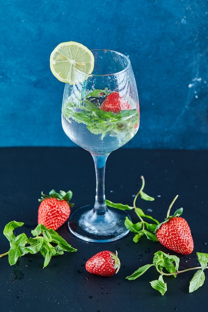 Un verre de jus avec des fruits entiers et une tranche de citron à l'intérieur sur une surface sombre