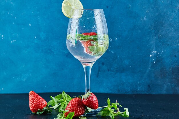 Un verre de jus avec des fruits entiers et une tranche de citron à l'intérieur sur une surface sombre