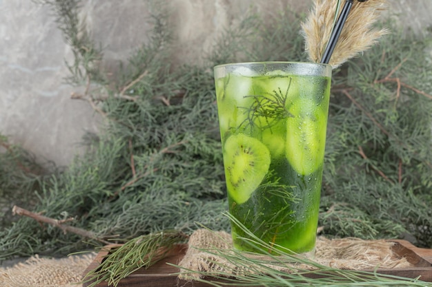 Photo gratuite un verre de jus de fruits avec des tranches de kiwi sur une plaque en bois