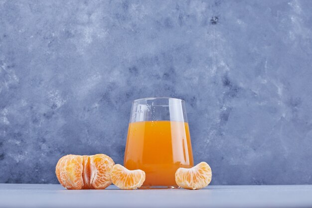 Un verre de jus de mandarine avec des fruits autour.