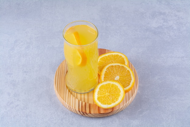 Un verre de jus d'orange à côté d'une tranche d'orange sur une plaque en bois sur une table en marbre.