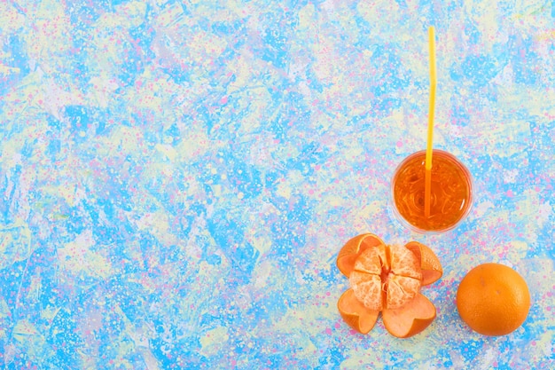 Un verre de jus d'orange avec des mandarines autour sur fond bleu, vue du dessus. Photo de haute qualité