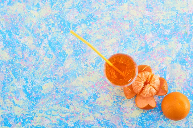 Un verre de jus d'orange avec des mandarines autour, vue du dessus