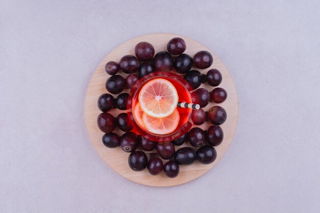 Un verre de jus rouge avec des baies de cerise sur une planche de bois