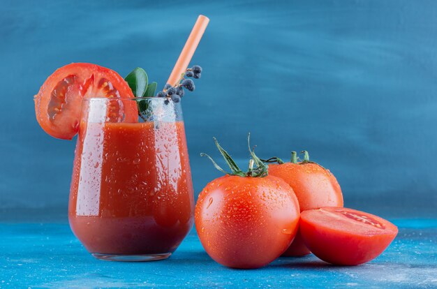 Un verre de jus de tomate et deux morceaux de tomates sur le fond bleu. Photo de haute qualité