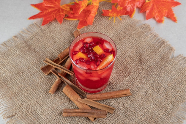 Verre de jus avec tranches de fruits et bâtons de cannelle sur toile de jute.