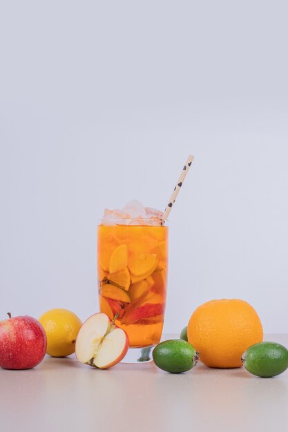 Un verre de jus avec des tranches de fruits et des fruits frais.