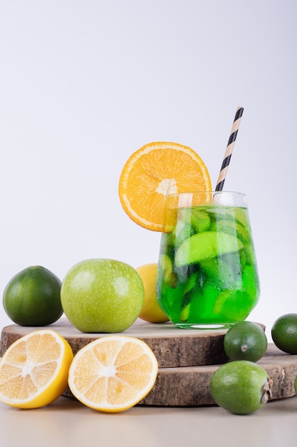 Un verre de jus avec des tranches de fruits et des fruits frais.