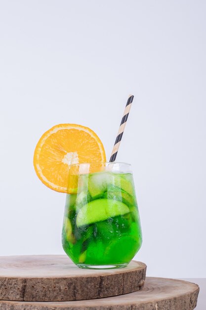 Un verre de jus avec des tranches de fruits sur un mur blanc.