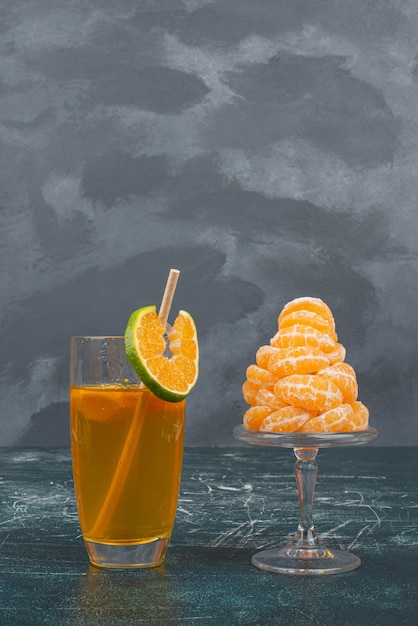 Verre de jus et tranches de mandarine sur mur de marbre.