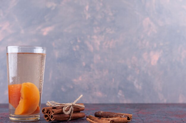 Verre de jus avec des tranches de poire et des bâtons de cannelle sur fond de marbre.