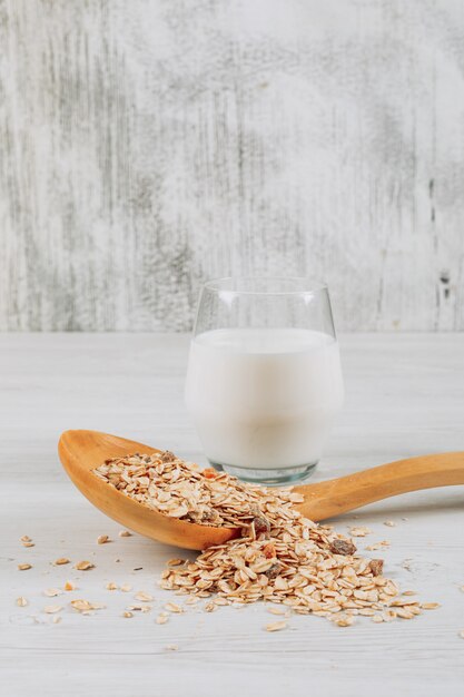 Verre de lait avec de l'avoine en vue de côté de cuillère en bois sur un fond en bois blanc