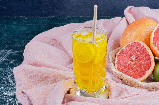 Un verre de limonade avec des tranches de citron et des pamplemousses sur une surface en marbre.