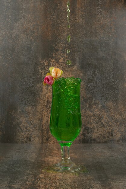 Un verre de limonade verte juteuse et de roses sur une surface en marbre.