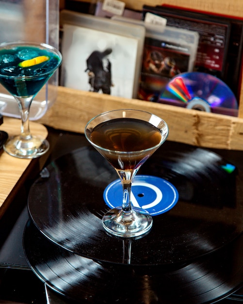 Un verre à martini avec cocktail de couleur foncée placé sur disque vinyle