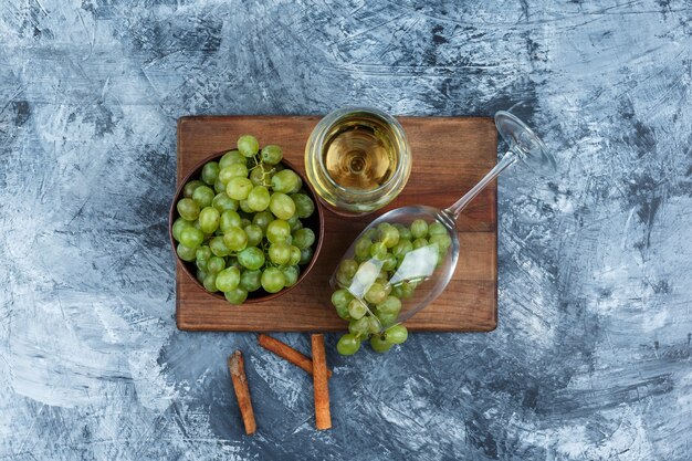 Photo gratuite verre à plat de whisky, raisins blancs sur une planche à découper avec de la cannelle sur fond de marbre bleu foncé. horizontal