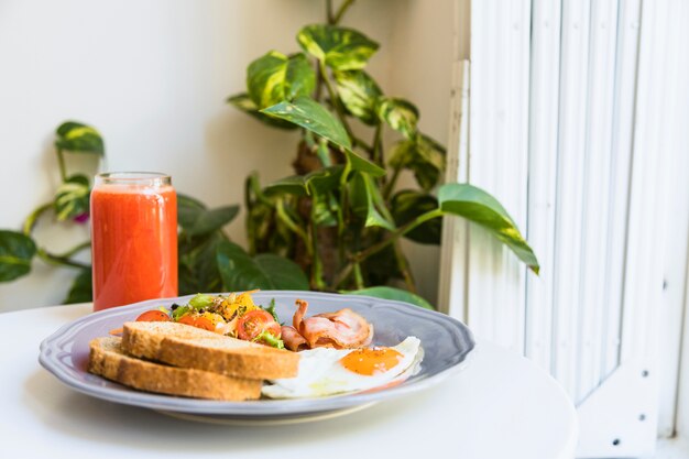 Verre sain de smoothies au bacon; salade; bacon et œufs sur le plat sur une plaque en céramique sur une table blanche