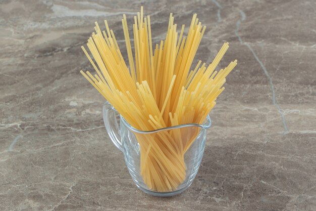 Verre de spaghettis non cuits sur une surface en marbre.