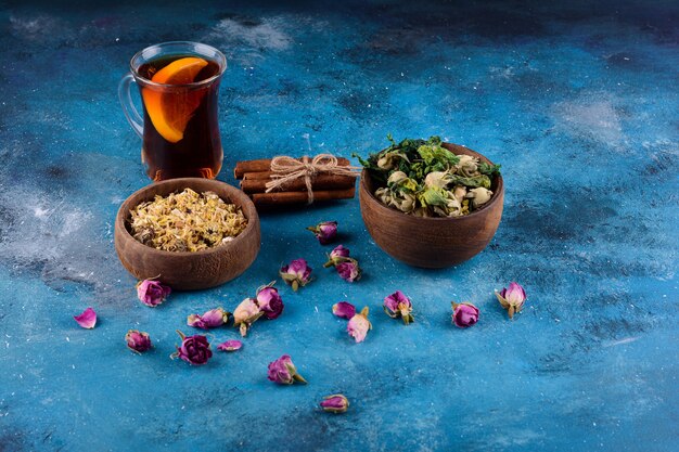 Verre de thé chaud avec des fleurs séchées sur table bleue.