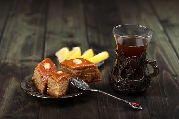 Un verre de thé avec pakhlava caucasien et citron sur une table rustique.