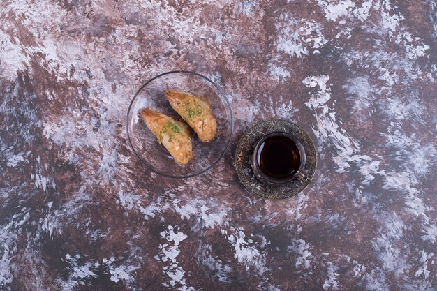 Un verre de thé avec pakhlava turque dans une soucoupe en verre au milieu.