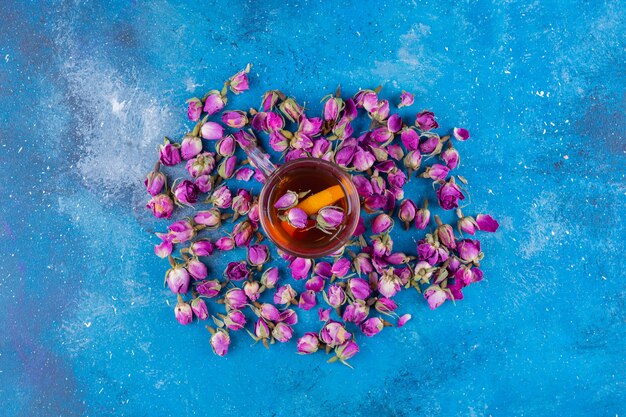 Verre de thé avec des roses en herbe placé sur une table bleue.