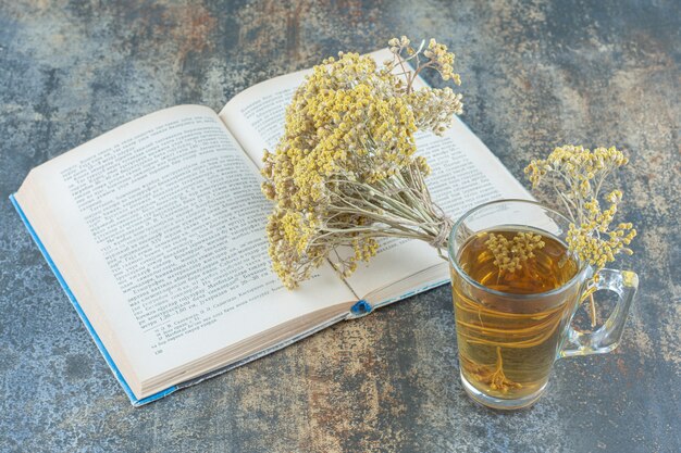 Verre de thé vert, livre et fleurs sur fond de marbre.