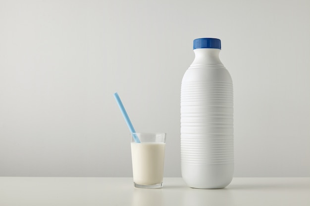 Verre transparent avec du lait frais et de la paille bleue à l'intérieur près d'une bouteille vide en plastique à rayures avec bouchon bleu