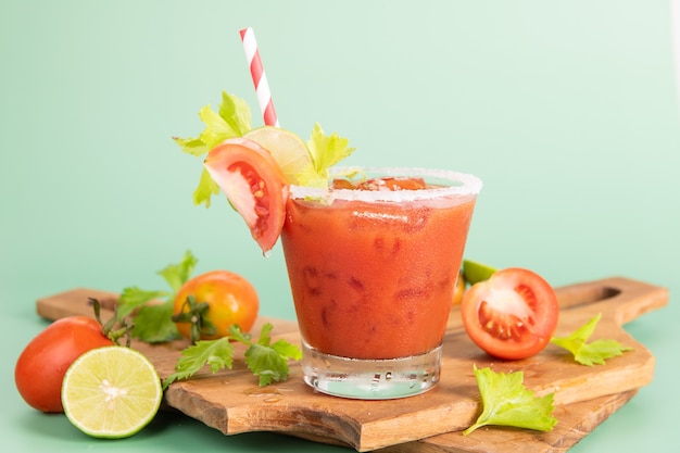 Verre en verre de jus de tomate, citron vert avec un bouquet de tomates fraîches et lumineuses isolé sur fond vert, persil vert. boisson végétale.