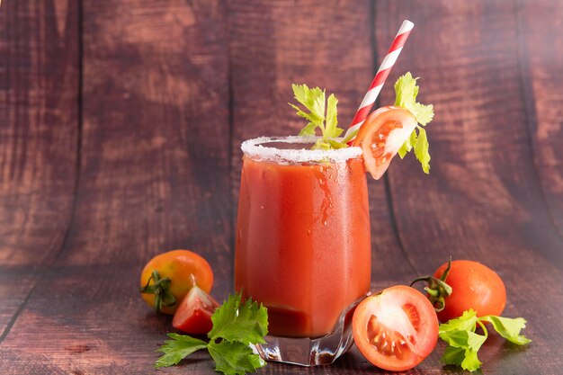 Verre en verre de jus de tomate avec des tomates fraîches et lumineuses, du persil vert sur fond sombre. boisson végétale.