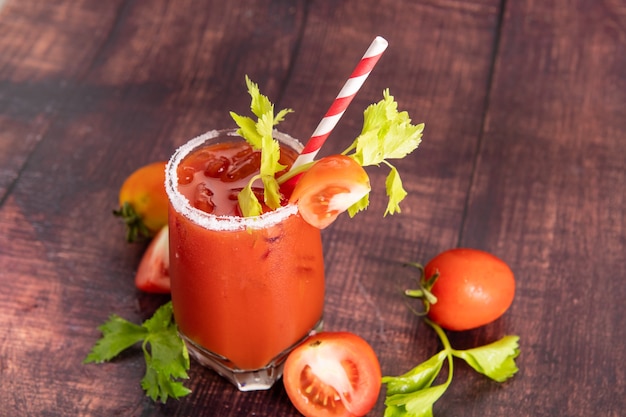 Verre en verre de jus de tomate avec des tomates fraîches et lumineuses, du persil vert sur fond sombre. boisson végétale.