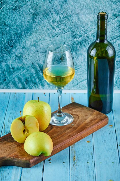 Un verre de vin blanc et une bouteille avec des tranches de pomme sur un mur bleu.