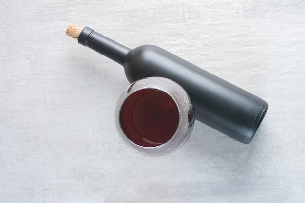 Un verre de vin avec une bouteille sur une surface blanche
