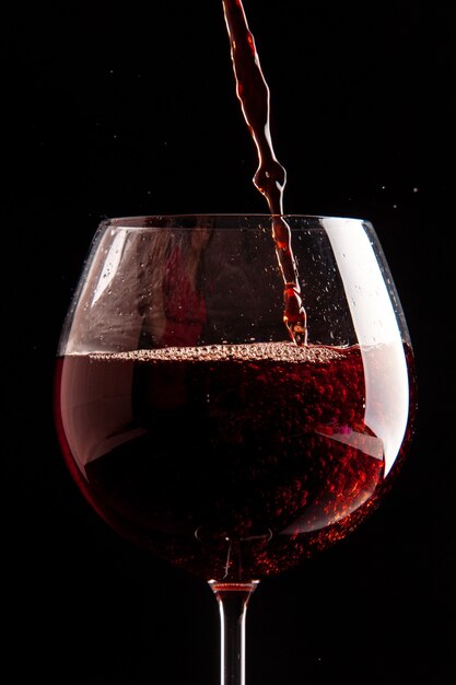 Verre à vin vue de face se verse avec du vin rouge sur une boisson alcoolisée au champagne de couleur noire