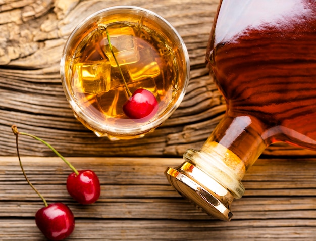 Verre à whisky vue de dessus avec glace et cerises et bouteille