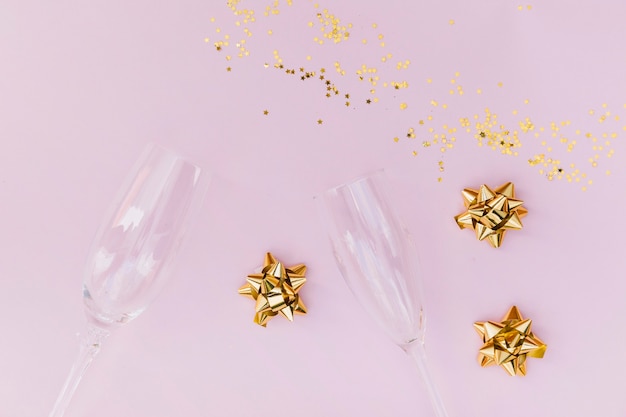 Photo gratuite verres de champagne transparents; arc doré et confettis sur fond rose
