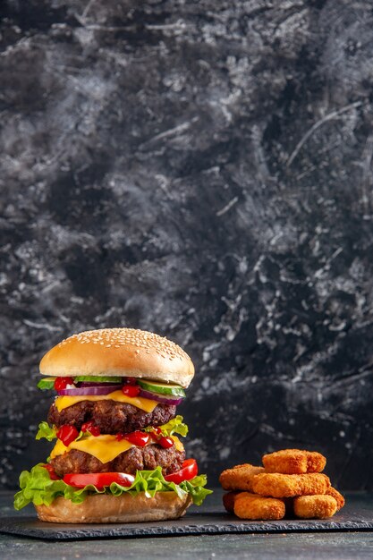 Vertica vue de savoureux sandwich à la viande avec des tomates vertes sur un plateau de couleur foncée et des pépites de poulet sur une surface noire
