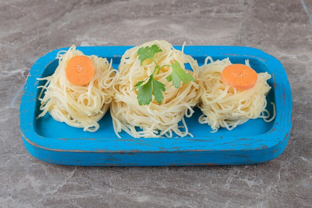 Photo gratuite verts et carottes râpées sur des spaghettis, sur la planche de bois, sur la surface en marbre.