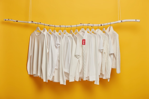Vêtements blancs à la mode sur des cintres avec étiquette rouge vente inscrite, accroché sur un support en bois sur fond jaune, copiez l'espace.