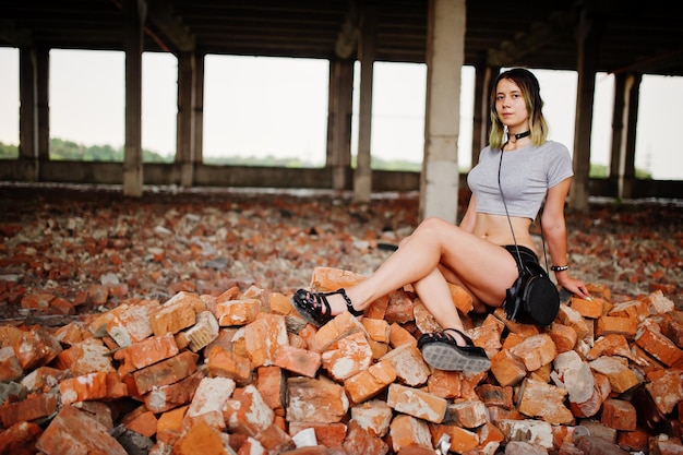 Photo gratuite vêtements de fille sur des shorts à l'usine abandonnée assise sur la brique